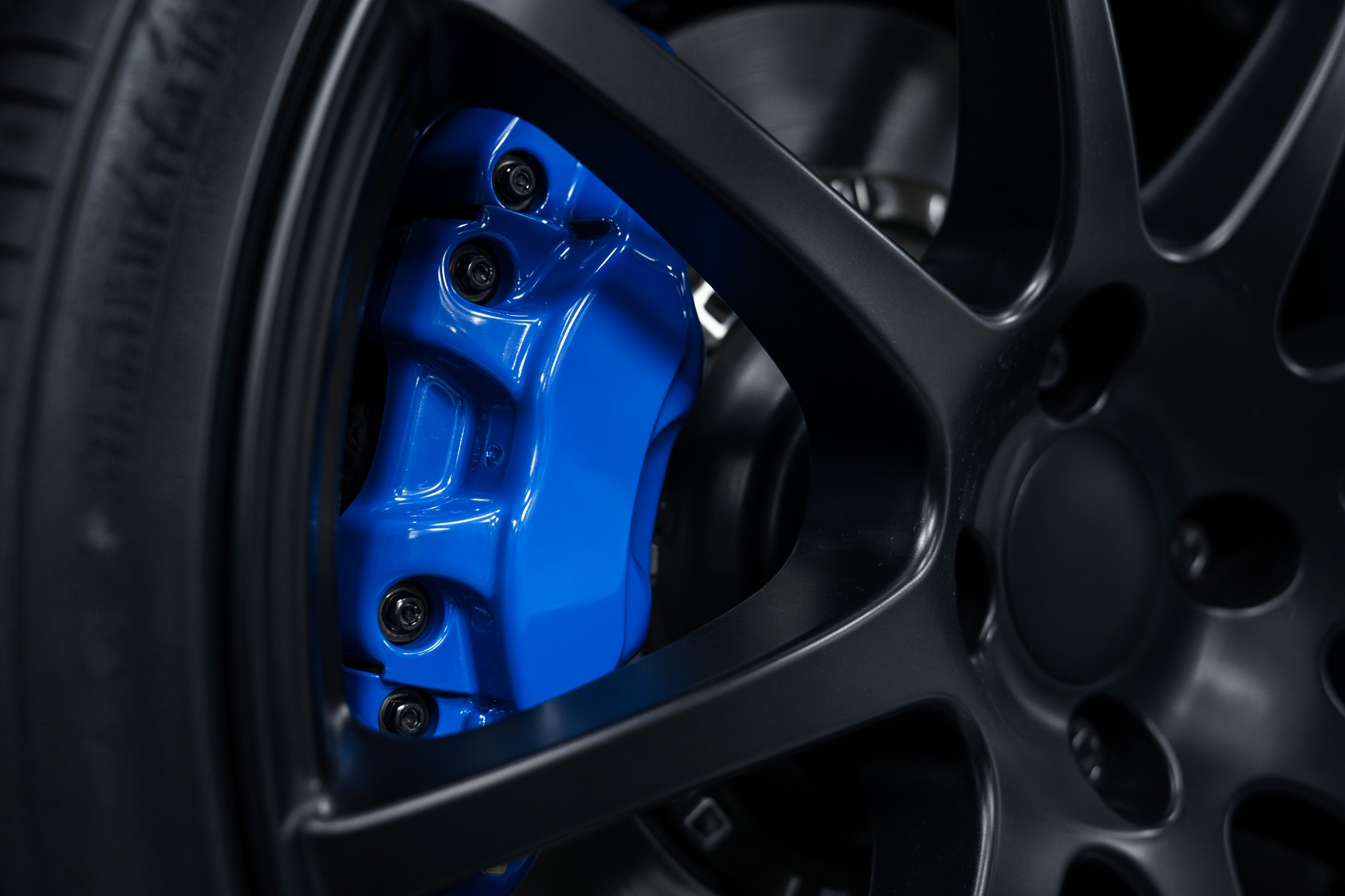 Freshly painted electric-blue brake caliper behind a black wheel